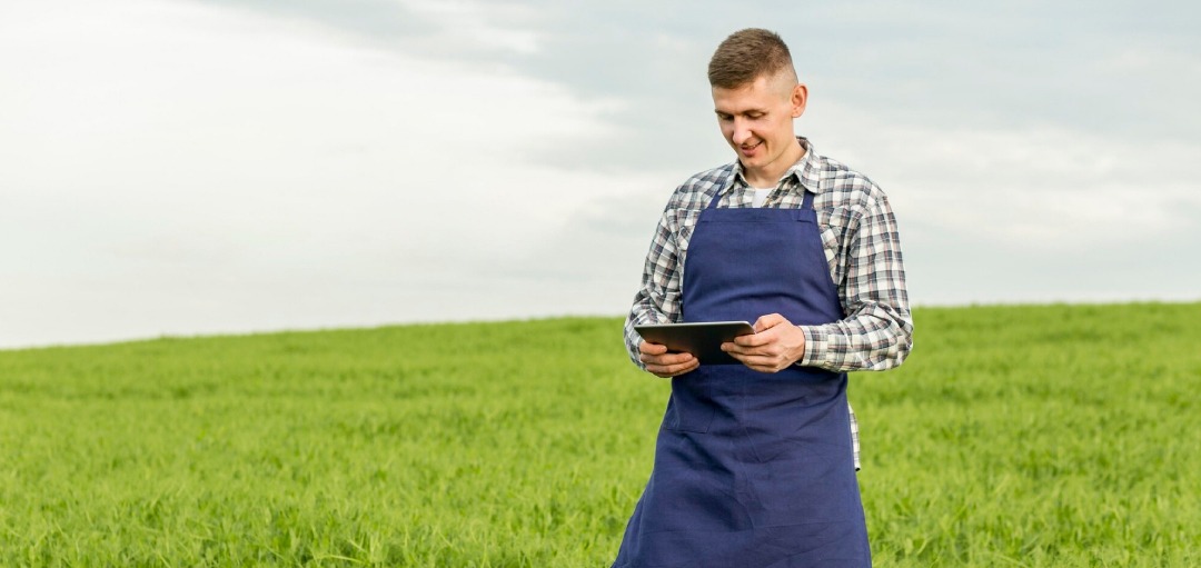 Jeune agriculteur sur une tablette tactile dans un champs d'herbe